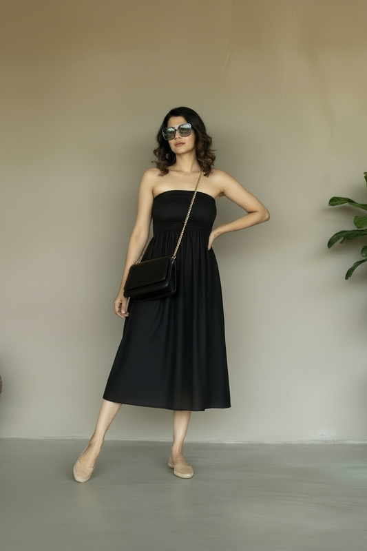 Woman in a black strapless dress holding a black clutch against a plain background