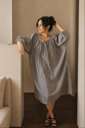 Woman wearing a navy and white checkered dress in a minimalistic room.
