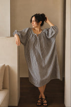 Woman wearing a navy and white checkered dress in a minimalistic room.