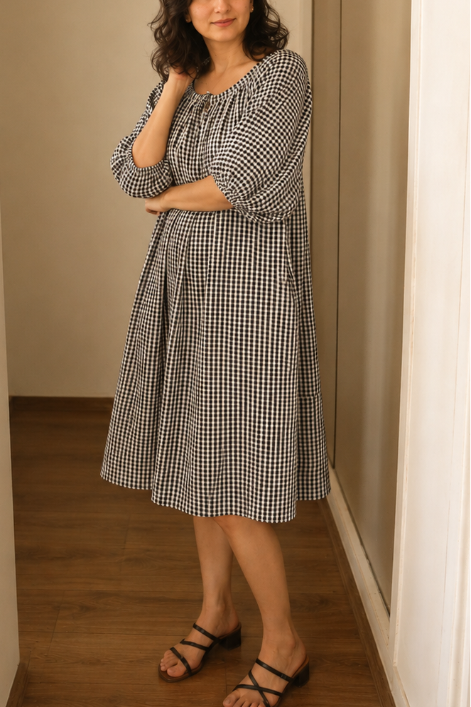 Woman wearing Blue Drift Midi Dress in Navy & White Check Cotton standing in a room with wooden floor and beige walls.