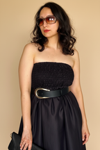 Woman wearing Blue Hour Black Linen Strapless Midi Dress with a belt against a beige background