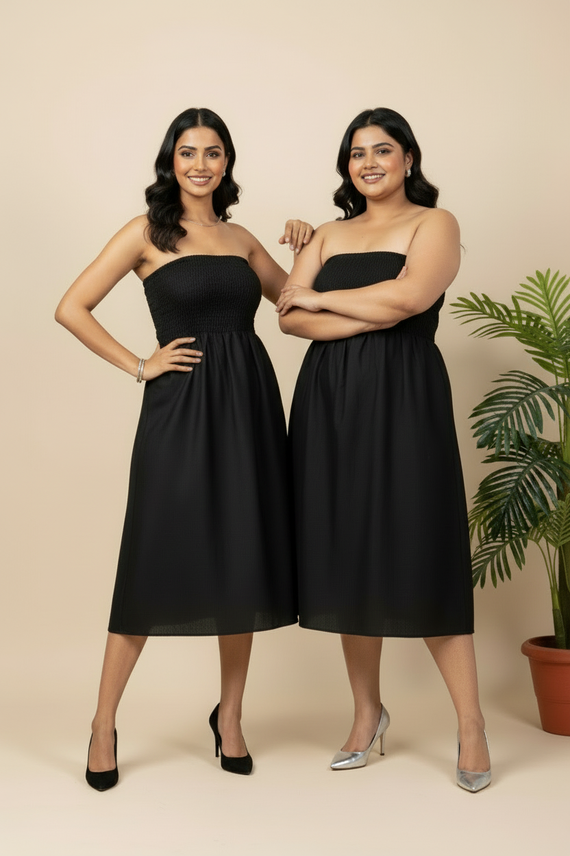 Two women wearing black strapless dresses standing against a beige background with a plant.