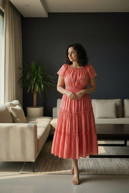 Woman in a coral midi dress made with pure mul cotton fabric standing in a modern living room with dark tone interior.