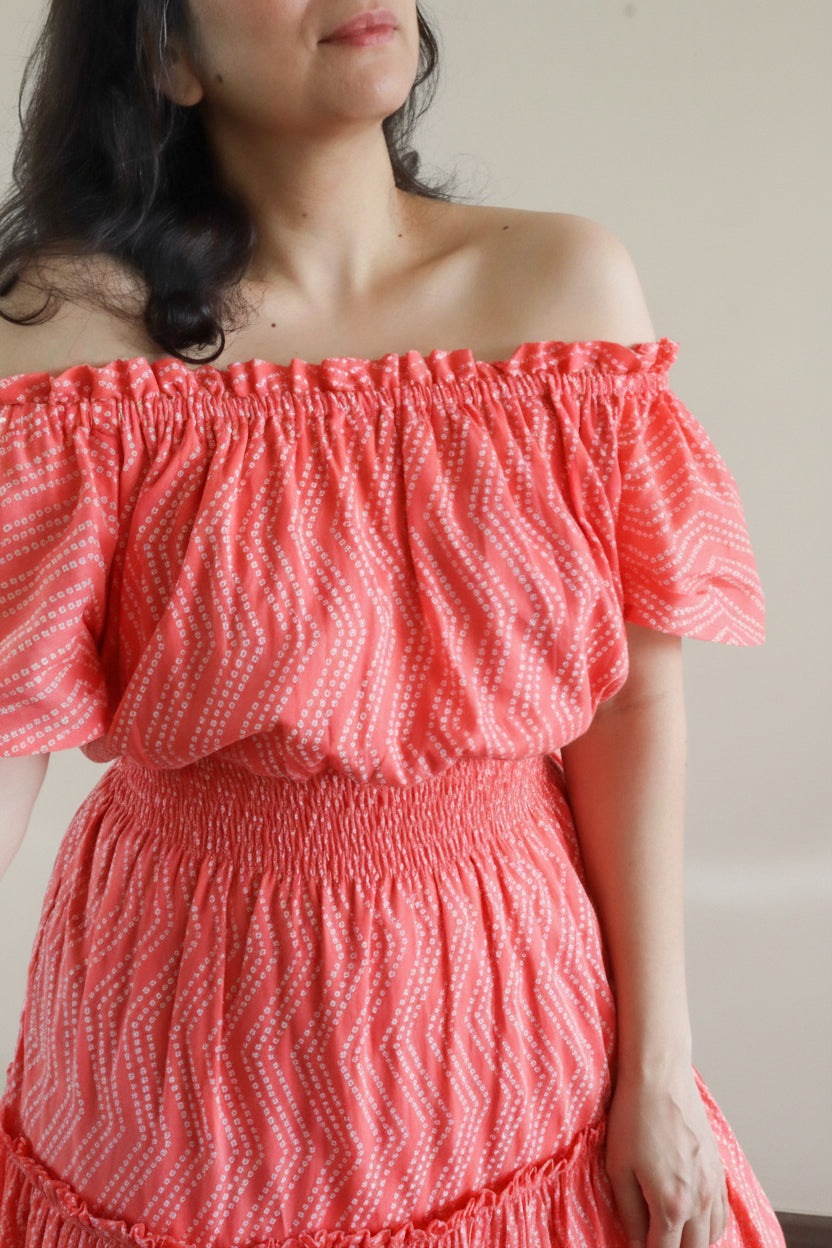 Woman wearing Coral Peach Mulmul Cotton Tiered Midi Dress off-shoulder. Showcasing the details like shirred waist and elasticated neckline in a closeup.