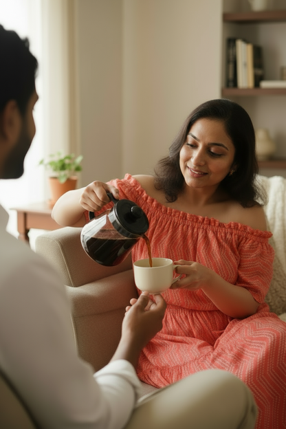 Woman in a pink dress pouring coffee into a cup held by a person in a living room.