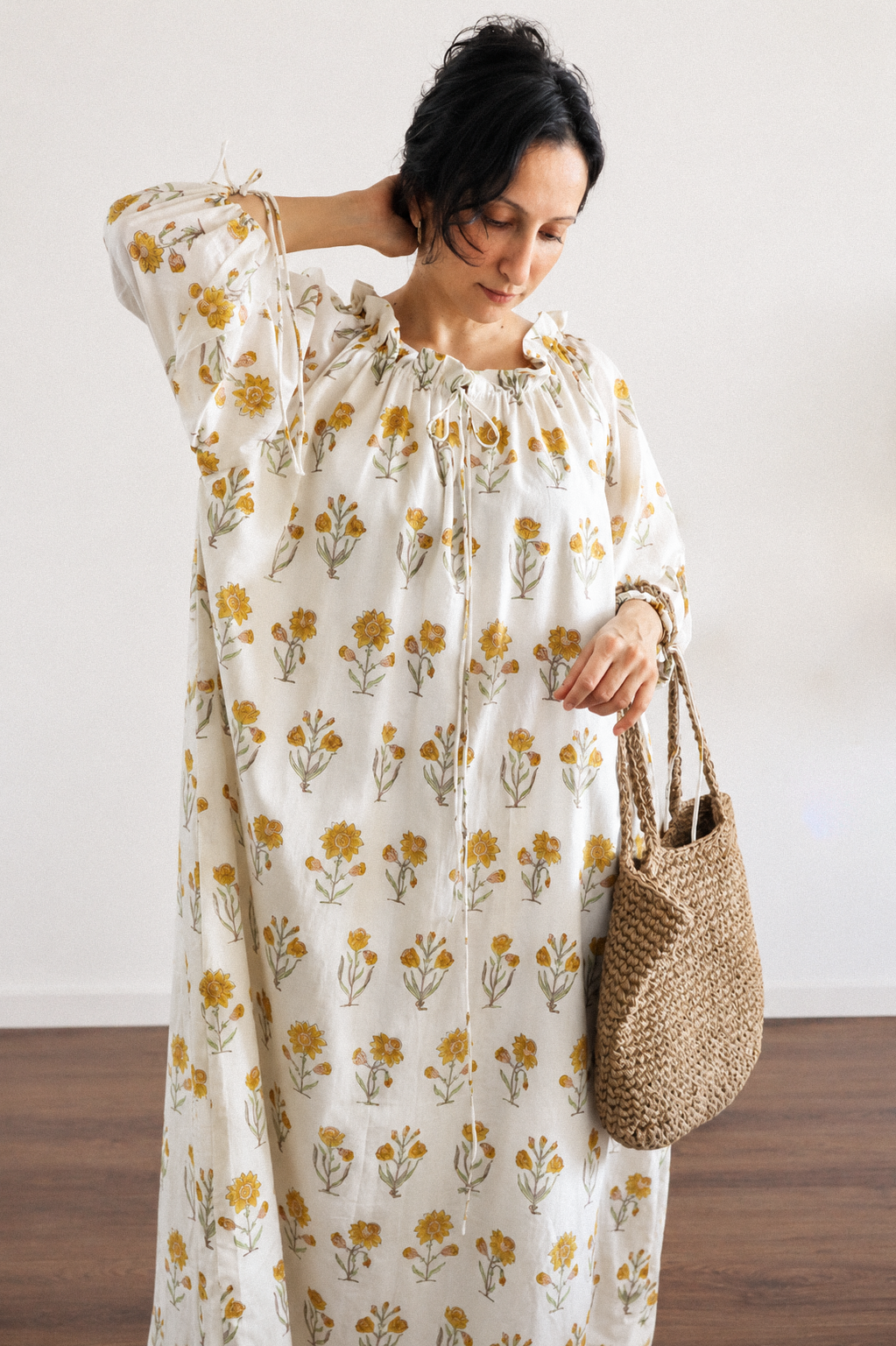 Woman wearing daydream floral maxi dress with cream base and small yellow flower all over. dress has neck tie and ties around the cuffs for ease of wearing. 
