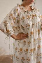 Close up of woman wearing daydream floral maxi dress with cream base and small yellow flower all over. She shows the close up of dress that has neck tie and ties around the cuffs for ease of wearing. 