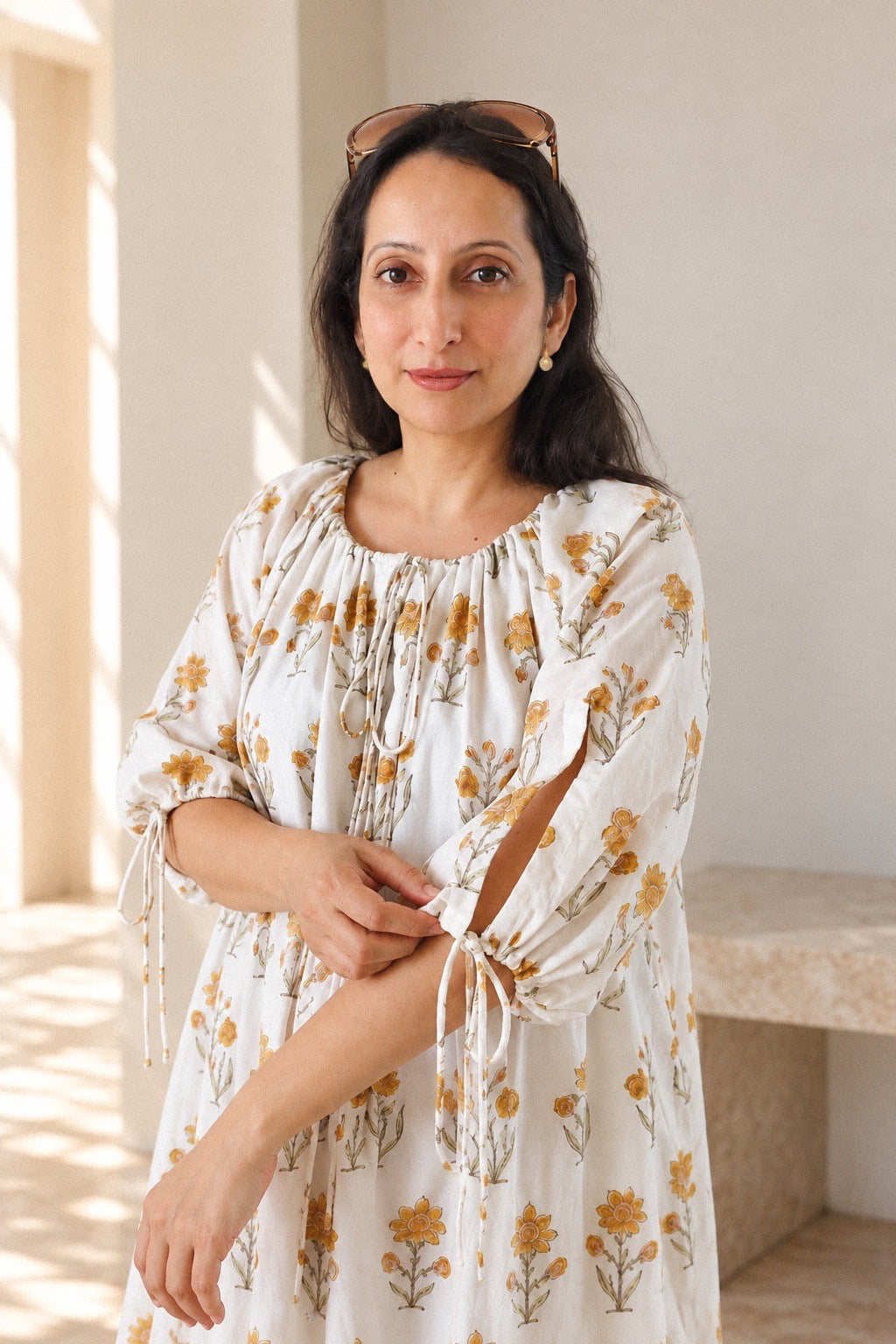 A woman models Daydream Cream Floral midi dress, cream-colored, long-sleeved midi dress with a yellow floral pattern. Closeup to showcase the neck and sleeve tie details.