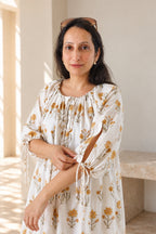 A woman models Daydream Cream Floral midi dress, cream-colored, long-sleeved midi dress with a yellow floral pattern. Closeup to showcase the neck and sleeve tie details.