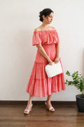 Woman in Flamingo Pink Mulmul Cotton Tiered Midi Dress, holding a white clutch against a plain background