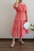 Woman wearing Flamingo Pink Mulmul Cotton Tiered Midi Dress off-shoulder holding a white bag indoors.
