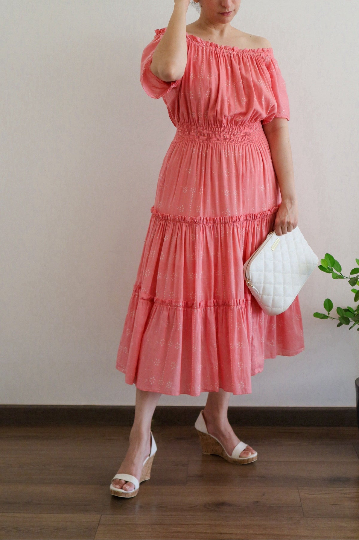 Woman wearing Flamingo Pink Mulmul Cotton Tiered Midi Dress off-shoulder holding a white bag indoors.