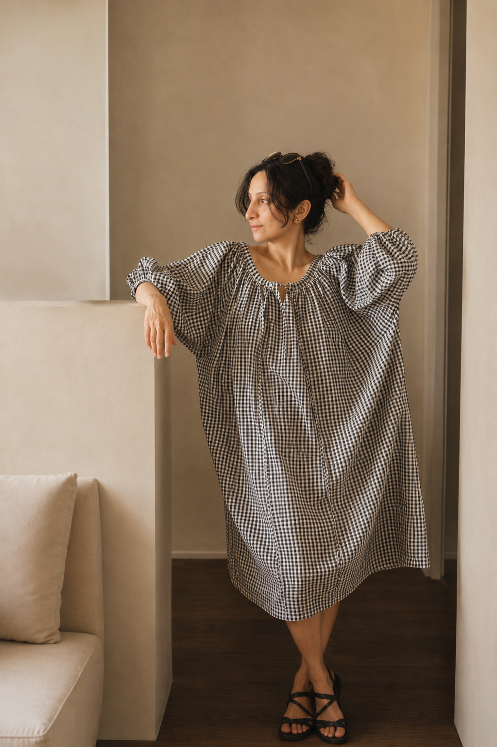 Woman in a checkered dress standing in a room with neutral walls and a couch.