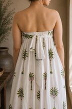 Woman wearing a strapless dress with palm tree patterns, showcasing the back that has elastic band and a tie for comfort of wearing in a warm-toned indoor setting.