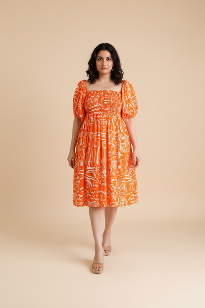 Woman wearing an orange patterned cotton midi dress with shirred bodice and puffed sleeves on a beige background