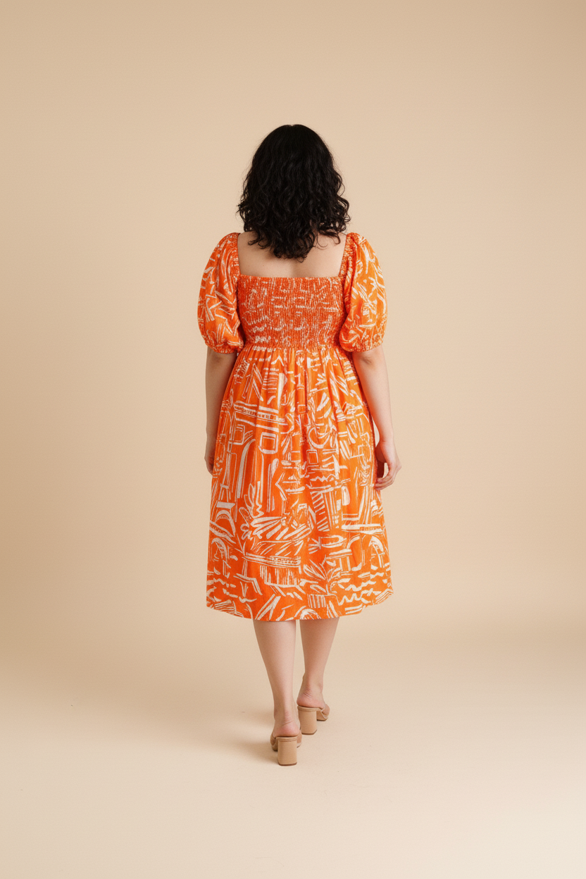 Woman wearing an orange patterned cotton midi dress with shirred bodice and puffed sleeves on a beige background