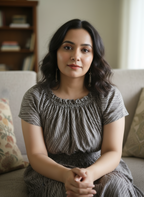 Woman in Seashell Grey Midi Dress in Mulmul Cotton, sitting on a couch in a home setting