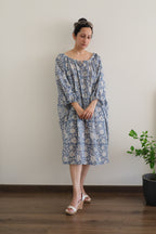 Woman in Still Blue Cotton Floral Midi Dress Puff Sleeve - Pastel Blue dress with gathered tie neckline.