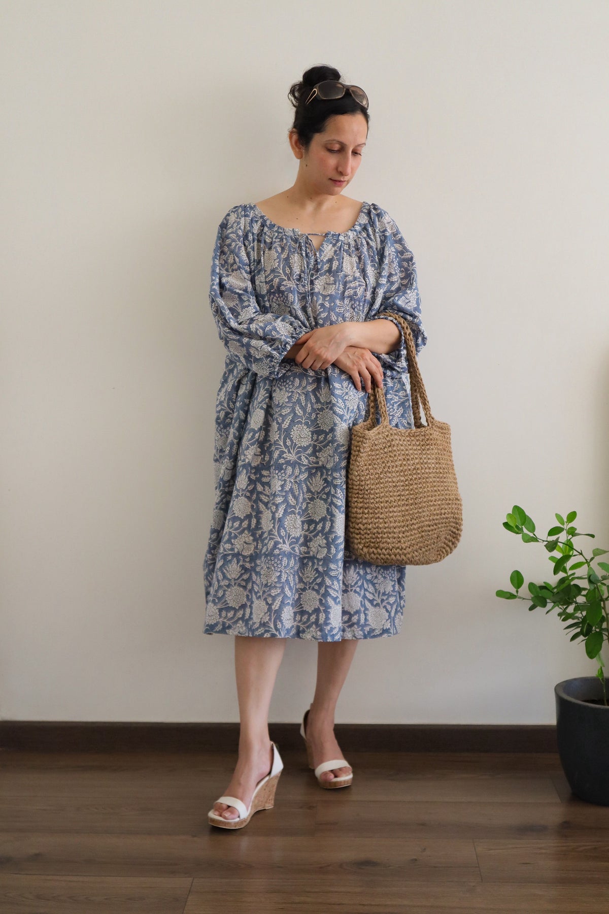 Woman in Still Blue Cotton Floral Midi Dress Puff Sleeve - Pastel Blue dress holding a woven bag indoors.