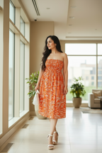 Woman in Sundown strapless midi dress in mulmul cotton with shirred bodice - front view, standing in a modern indoor setting with large windows.