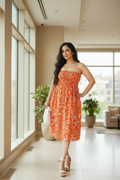Woman in Sundown strapless midi dress in mulmul cotton with shirred bodice - front view, standing in a modern indoor setting with large windows.