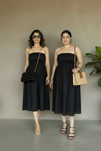 Two women wearing black strapless dresses standing against a plain background.