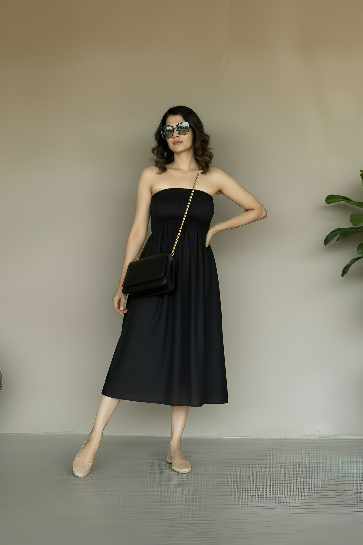 Woman in a black strapless dress, with shirred bodice, holding a black clutch standing against a plain stucco background