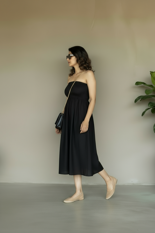 Woman in a black strapless dress standing against a plain wall with a plant in the corner.