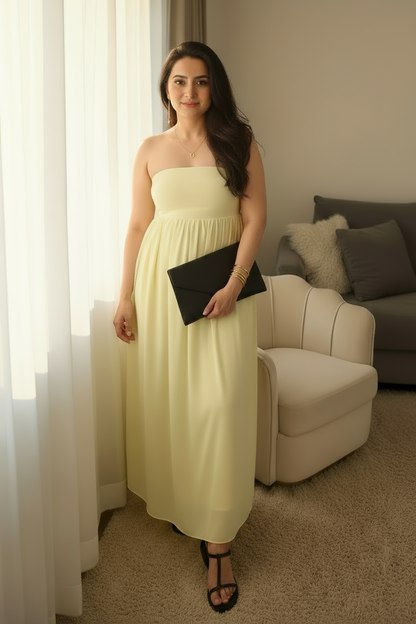 Woman in a light yellow dress holding a black clutch in a living room.
