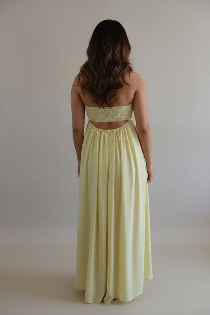 Woman wearing a light yellow strapless dress against a plain background